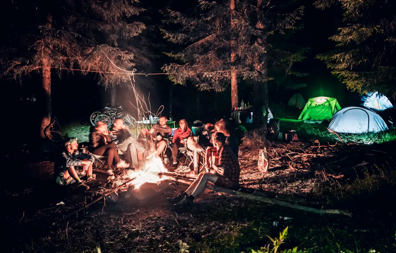 A group of campers gathered around an evening campfire with tents in the background
