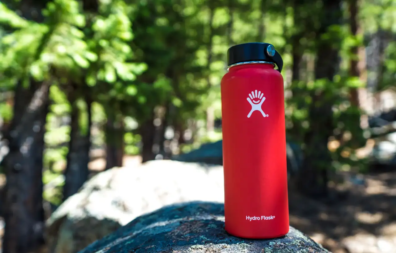 A red refillable water bottle resting on a sunlit rock outdoors